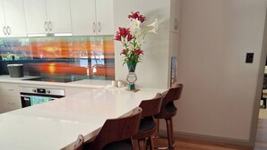 A modern kitchen with a large island, wooden bar stools, and a vase of flowers. - The Anunaka on Wadandi Boodja (Margaret River)