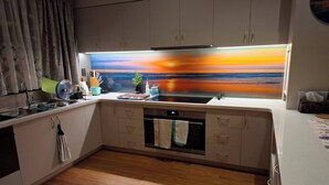 A modern kitchen with wooden flooring, a built-in oven, and a large window with a sunset view. - The Anunaka on Wadandi Boodja (Margaret River)