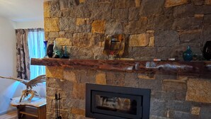 A stone fireplace with a wooden mantel, a framed mirror, and decorative items. - The Anunaka on Wadandi Boodja (Margaret River)