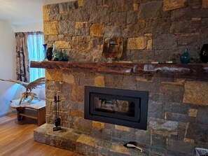 A stone fireplace with a wooden mantel, a framed mirror, and decorative items. - The Anunaka on Wadandi Boodja (Margaret River)