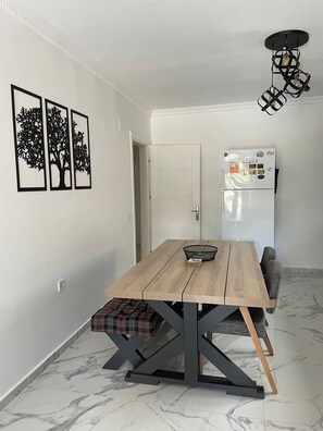 A dining area with a wooden table, a bench, a refrigerator, and wall art. - Sylvana Apartment- a little piece of Kalkan heaven (Kalkan)