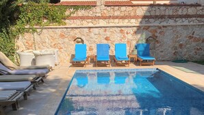 Una piscina con sillas reclinables azules y un muro de piedra.
