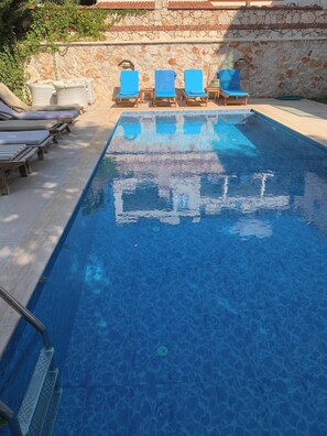 A swimming pool with blue lounge chairs and a stone wall. - Sylvana Apartment- a little piece of Kalkan heaven (Kalkan)