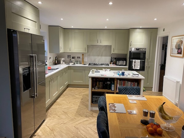 A modern kitchen with built-in appliances, a central island with seating, and a dining table.