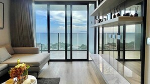 Un soggiorno moderno con un divano, un tavolino da caffè con fiori e un'ampia porta scorrevole in vetro che dà su un balcone con vista sul mare.