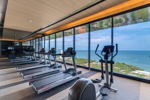 Une salle de sport équipée de tapis de course et d’appareils elliptiques, avec de grandes fenêtres offrant une vue sur la mer.