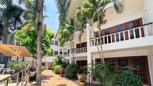 A courtyard with a tiled walkway, palm trees, potted plants, and outdoor seating. - Modern Ground Floor Suite with Shared Pool (Tambon Patong)