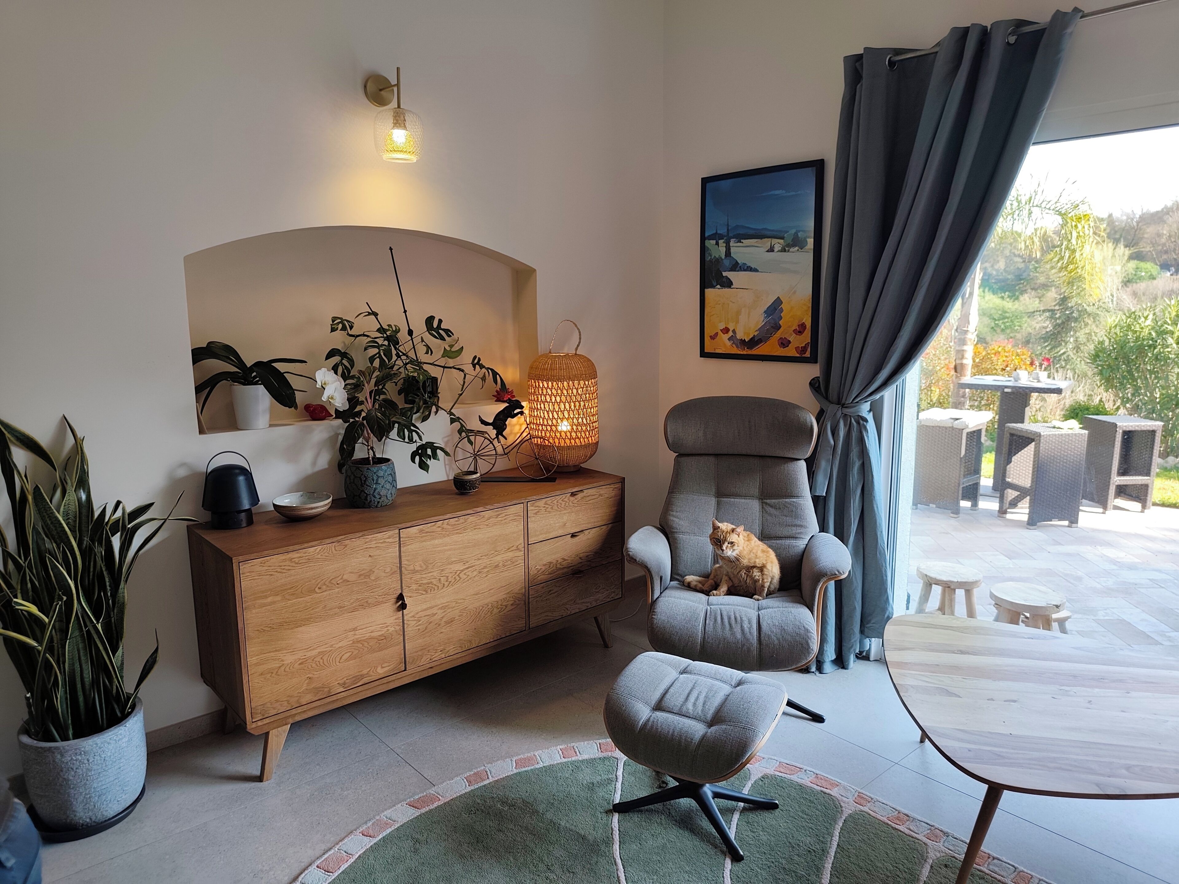 Ein Wohnzimmer mit Sofa, einem Sessel, einem Holzschrank, einer Topfpflanze, einer Lampe und einem Gemälde.
