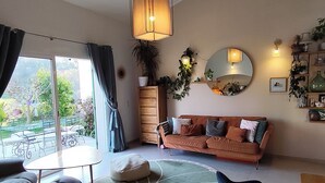 A living room with a sofa, chairs, a dining table, a large window, a hanging light fixture, and a mirror on the wall. - Provençal villa, swimming pool and wooded garden in a quiet location (Vence)