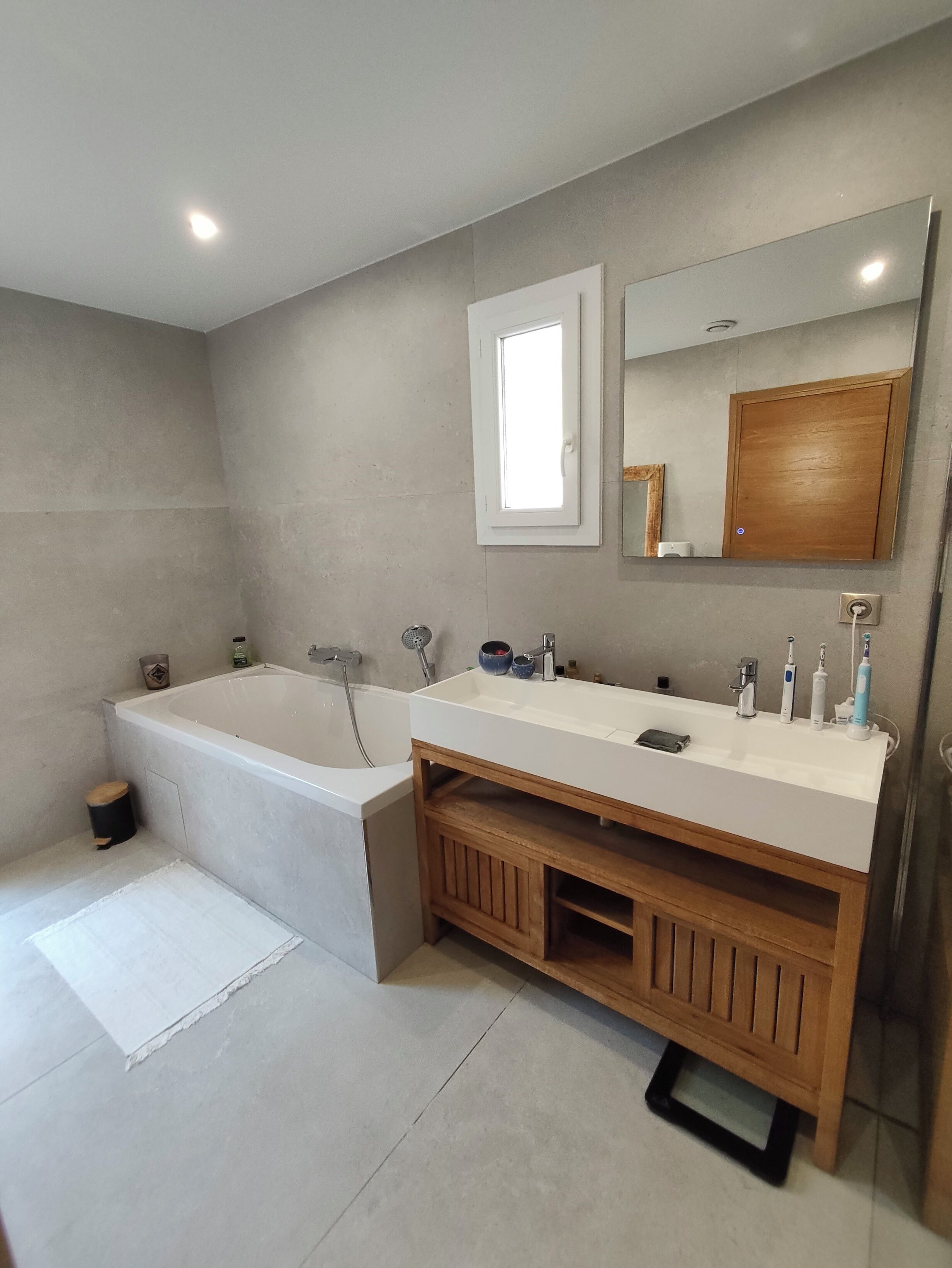 A modern bathroom with a bathtub, a large mirror, and a vanity with a sink.