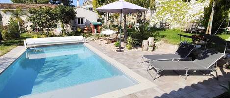 A rectangular swimming pool with a tiled deck, two lounge chairs, and a pergola with a canopy.