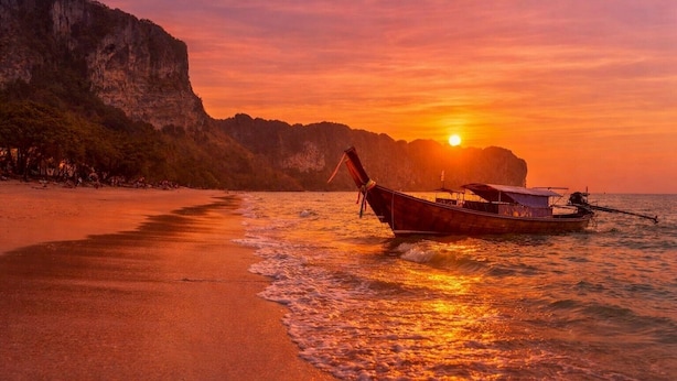 A boat on a beach with a sunset in the background. - Serene Suite with Balcony and Pool View (Tambon Patong)