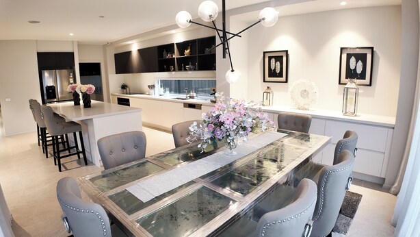 Una cocina moderna con una isla central, un comedor con mesa de vidrio y una isla con electrodomésticos integrados.