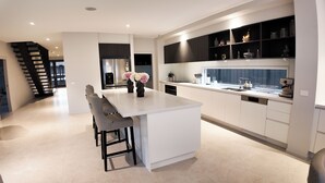 Una cocina moderna con una isla central, taburetes de bar y una escalera que lleva a otro nivel.