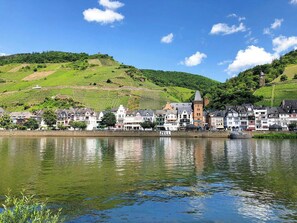 A riverside town with a prominent tower, vineyards, and a mix of traditional and modern buildings. - Holiday apartment Schwarze Katz in guesthouse in the old town of Zell (Moselle) (Zell (Mosel))