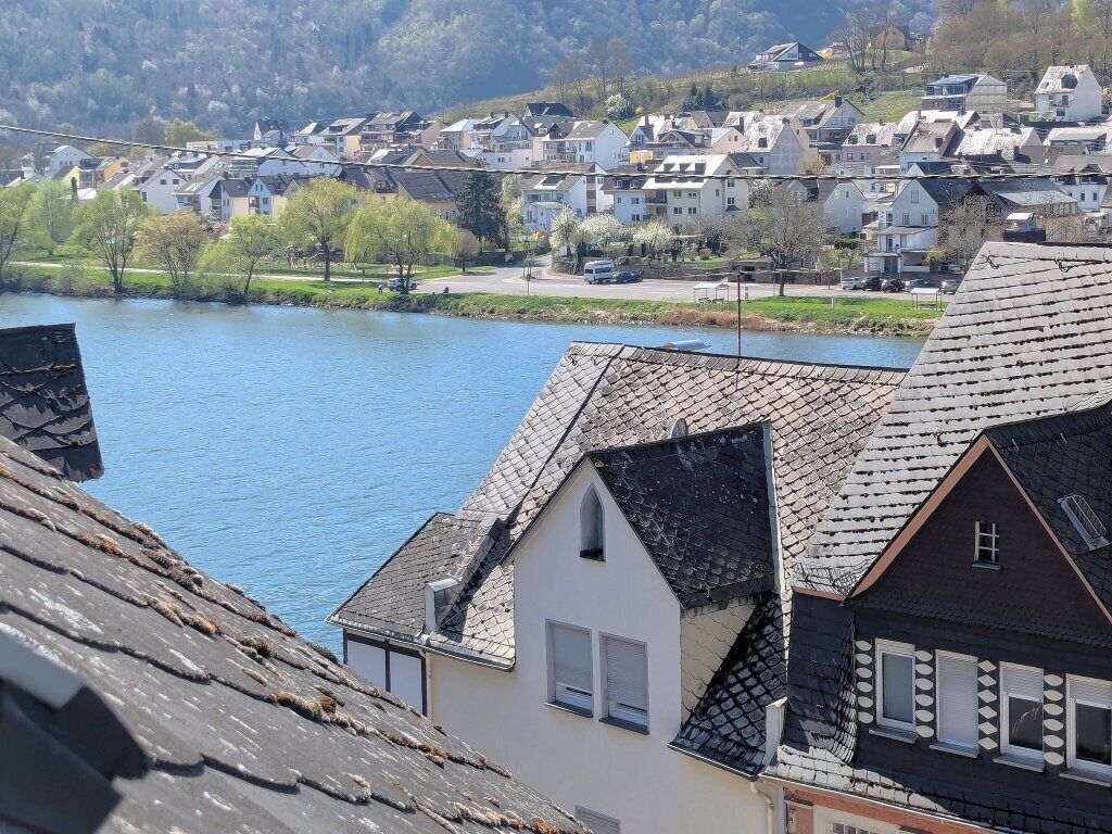 Un barrio residencial con casas a lo largo de un río, cielo despejado y colinas al fondo.
