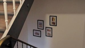 Eine Treppe mit weißen Balustern und einem hölzernen Geländer, die zu einer Zwischenebene mit gerahmten Bildern an der Wand führt.