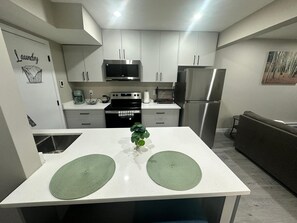A modern kitchen with white cabinets, stainless steel appliances, and a central island with green placemats. - Cozy 1-bedroom  Suite in Saskatoon -Fully Furnished near Industrial Area/Shops (Saskatoon)