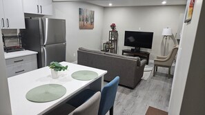 A compact kitchen with a refrigerator, dining table, and a television in the living area. - Cozy 1-bedroom  Suite in Saskatoon -Fully Furnished near Industrial Area/Shops (Saskatoon)