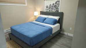A bedroom with a bed, a nightstand, a lamp, and a wall art piece. - Cozy 1-bedroom  Suite in Saskatoon -Fully Furnished near Industrial Area/Shops (Saskatoon)