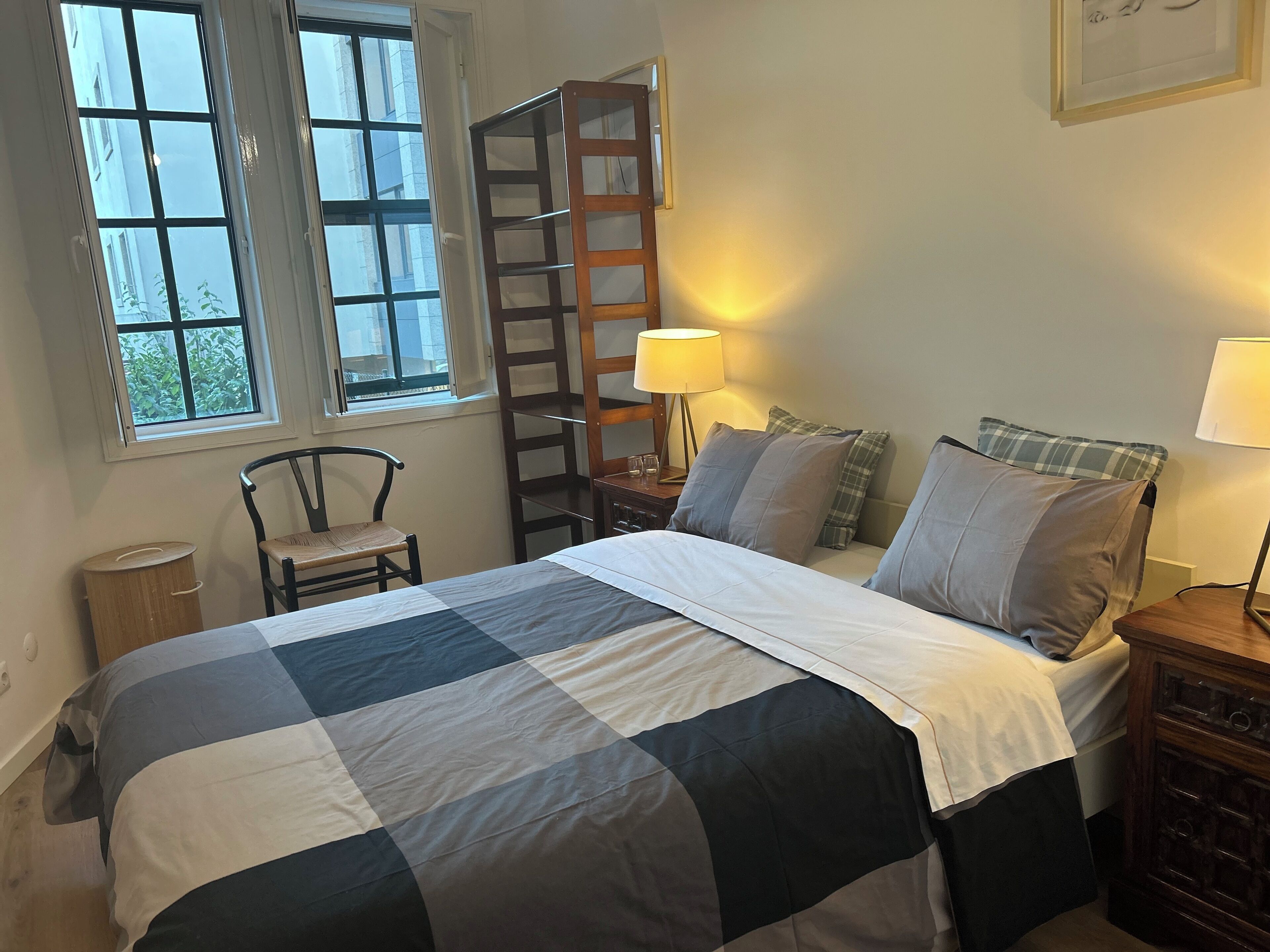 A bedroom with a bed, two bedside tables, a chair, a wooden ladder, and a window.