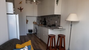 Moderni keittiö, jossa on keskeinen keittiösaareke, baarituolit sekä ruokailutila, jossa on sohva ja koristetyynyt.
