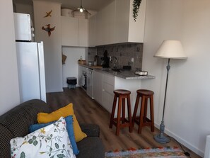 A modern kitchen with a central island, bar stools, and a dining area with a sofa and cushions. - Rosemary - Cozy and lots of natural light (Porto)