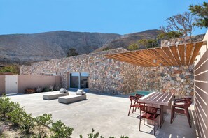 Eine Terrasse mit Steinmauer, Sitzgelegenheiten im Freien, einem Pool und Blick auf Berge.