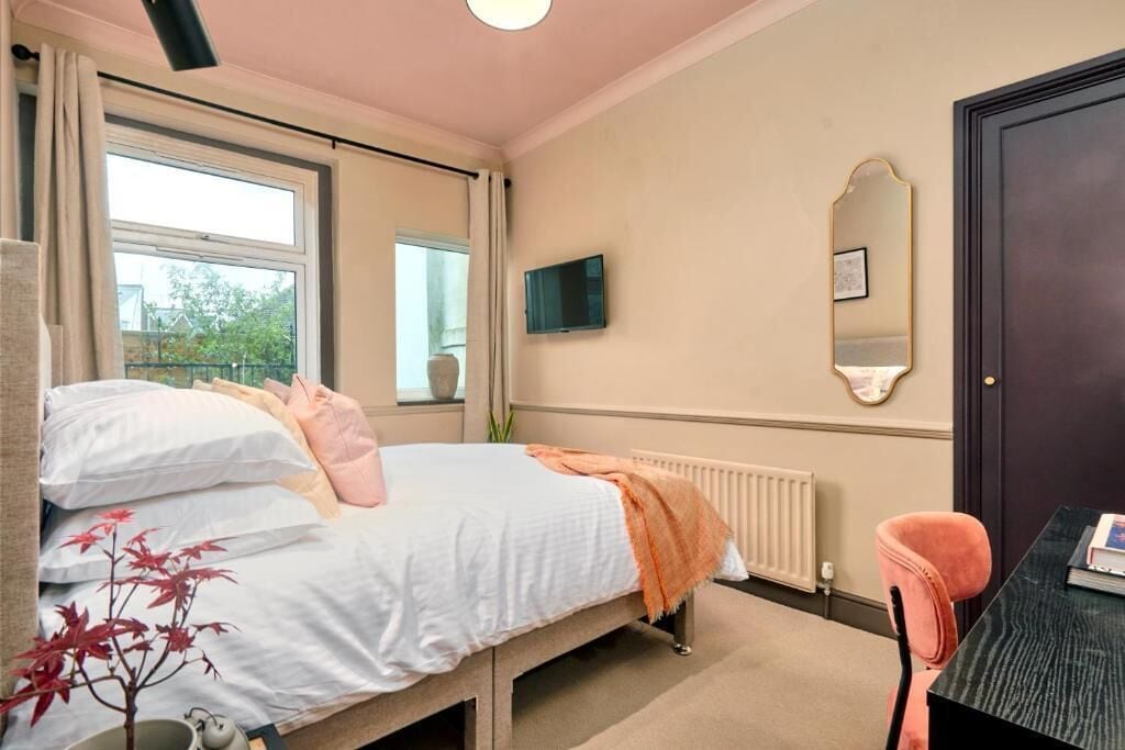 Un dormitorio con cama, escritorio, silla, radiador, televisor y ventana.