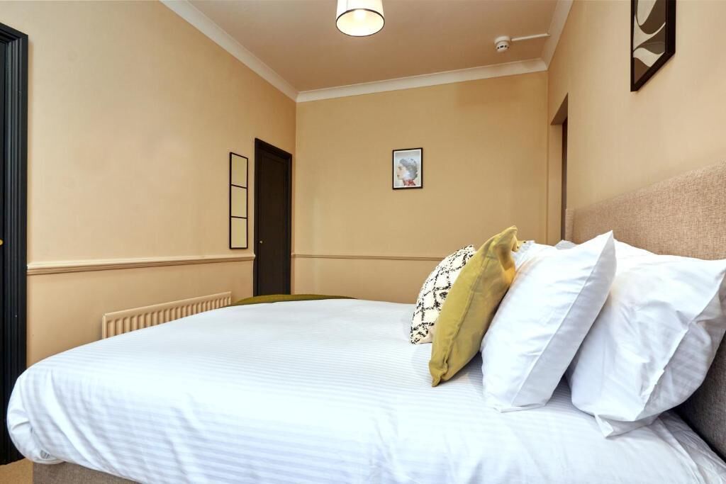 A hotel room with a large bed, a radiator, a framed picture on the wall, and a door.