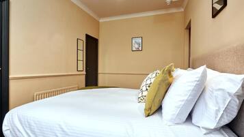 A hotel room with a large bed, a radiator, a framed picture on the wall, and a door.