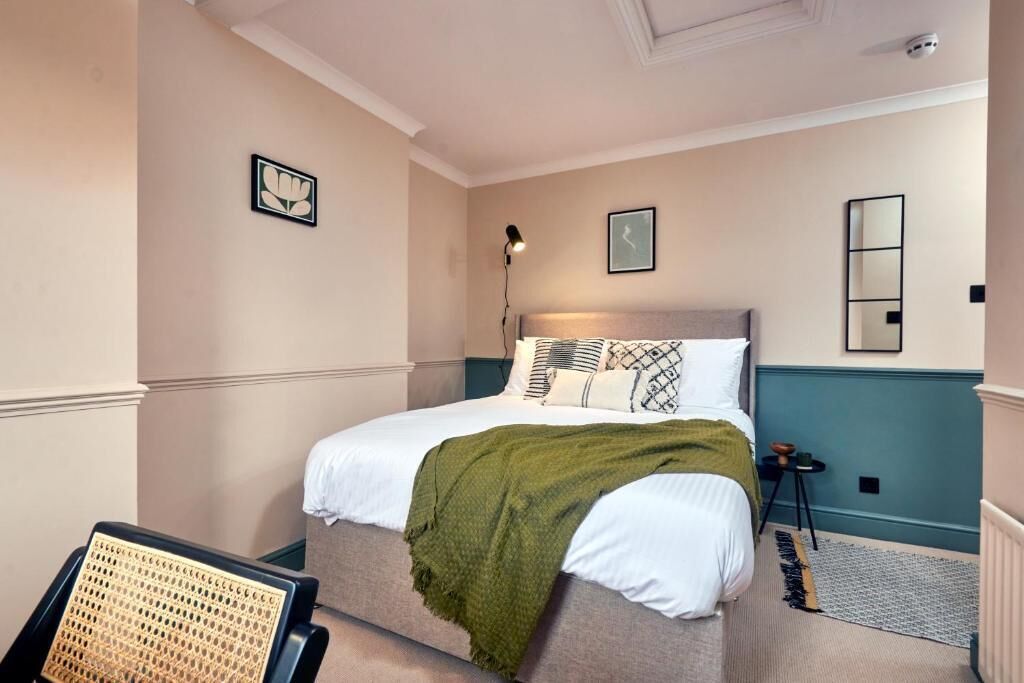 Un dormitorio con cama, mesita de noche, lámpara y espejo en la pared.