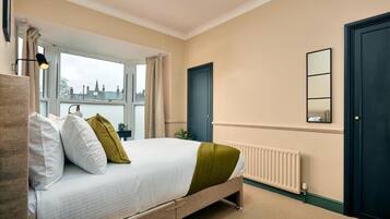 A bedroom with a bed, a window, a radiator, a door, and a mirror.