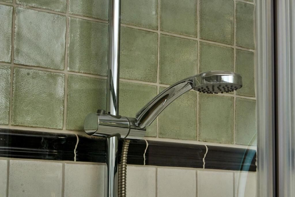 Un cabezal de ducha cromado fijado a una pared con revestimiento de azulejos.