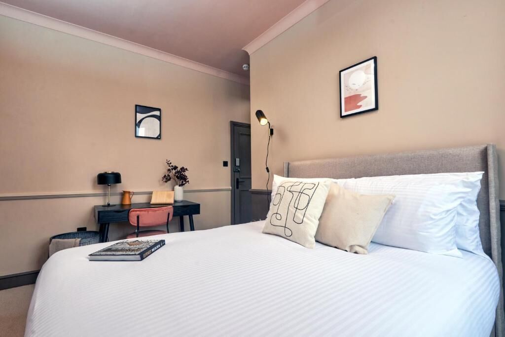 Habitación de hotel con una cama grande, un escritorio con silla, una lámpara y un cuadro en la pared.