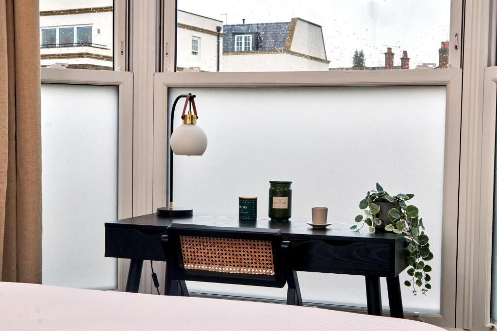 Una habitación con un escritorio, una lámpara, una planta y vistas a través de una ventana.