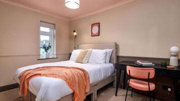 A bedroom with a bed, a desk, a chair, a window, and a wall-mounted light fixture.