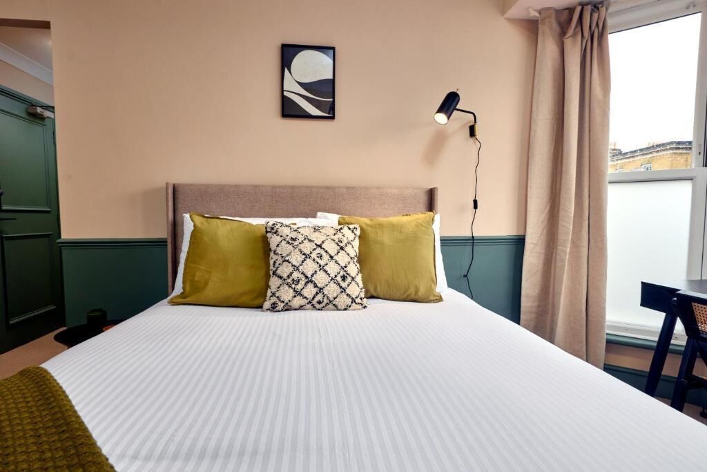 A hotel room with a bed, a desk, a lamp, and a view of the city.