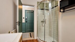 A bathroom with a glass-enclosed shower, a bathtub, and a door leading to another room. - Settle Winchester (Winchester)
