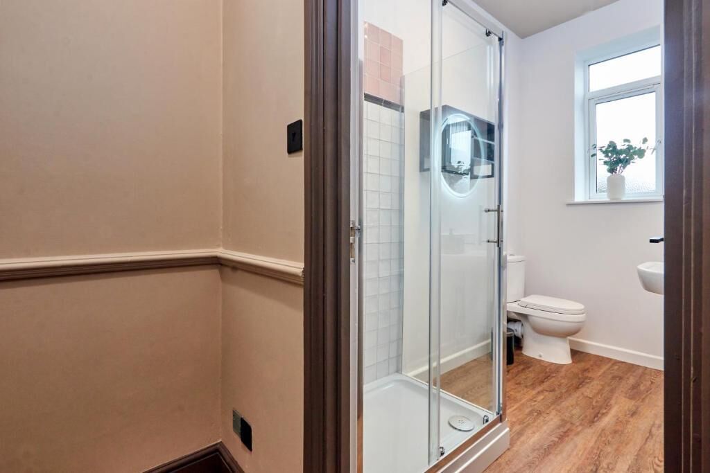 A bathroom with a glass shower enclosure, a toilet, a sink, and a window with a plant.