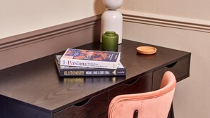 A dark wooden desk with a stack of books, a green vase, and a white lamp. - Settle Winchester (Winchester)