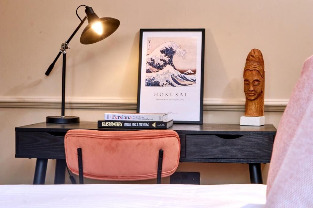 Un bureau agrémenté d’une œuvre d’art encadrée, une lampe, une chaise et une sculpture en bois.