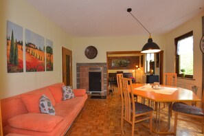 A living room with a sofa, a dining table with chairs, a fireplace, and wall art. - Ferienwohnung im Erholungsort (Steinbach-Hallenberg)