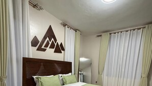 A neatly made bed with a wooden headboard, a bedside table with a clock, and a wall-mounted mirror. - Luxurious 1 BR Apt in quaint Kampala with power backup. (Kampala)