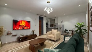 A modern living room with a flat-screen TV, a sofa, a coffee table, and a fireplace. - Luxurious 1 BR Apt in quaint Kampala with power backup. (Kampala)