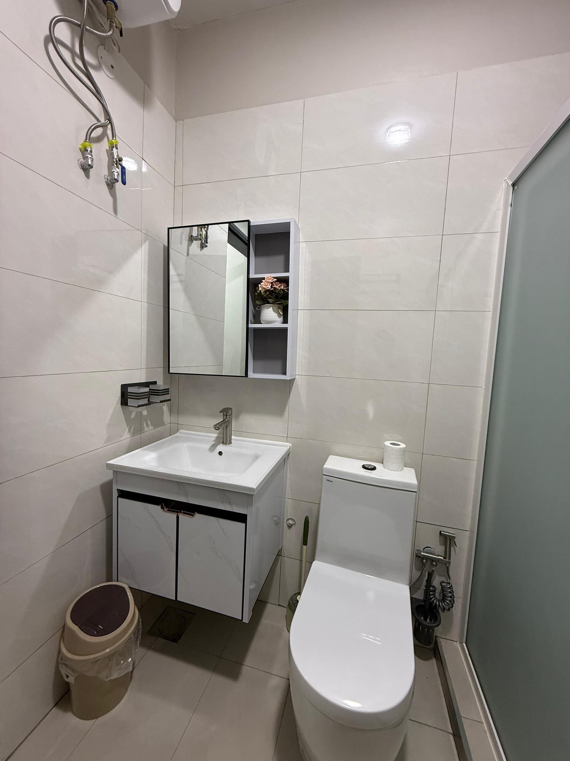 A bathroom with a white sink, mirror, toilet, and a small trash bin.