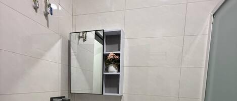 A bathroom with a white sink, mirror, toilet, and a small trash bin.