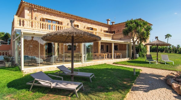 A large stone building with a glass-enclosed patio, outdoor seating, and lounge chairs.