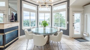 A dining area with a glass table surrounded by white chairs, a chandelier, and a view through large windows. - Ski, Hike & Bike: 4,000 Sq Ft Bell Canyon Retreat (Sandy)