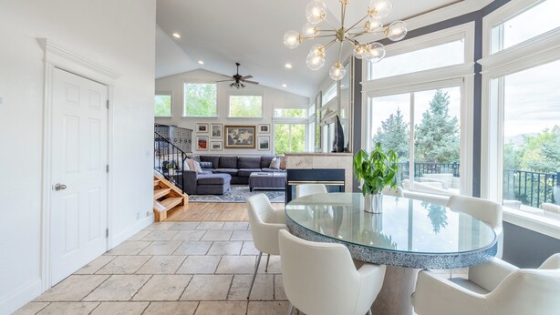 A spacious living area with a glass-top dining table, white chairs, a ceiling fan, and a large window with a view of trees. - Ski, Hike & Bike: 4,000 Sq Ft Bell Canyon Retreat (Sandy)